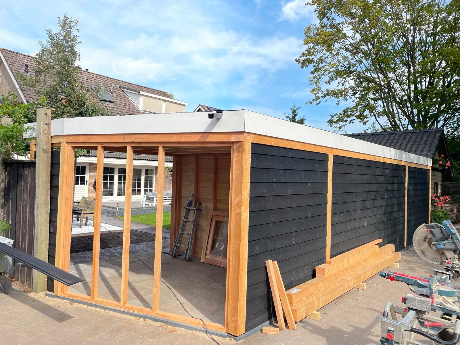 Vrijstaande houten overkapping met zwarte gevelbekleding in een tuin in Waalwijk